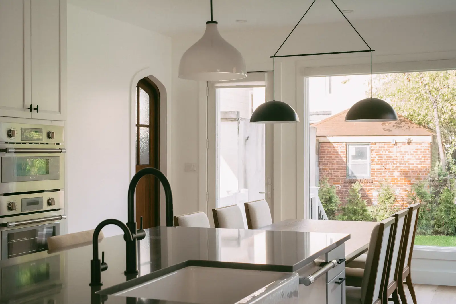 Renovated kitchen with arched wood door, matte black fixtures and pendant lighting — The Columbia Project by One Horizon Homes