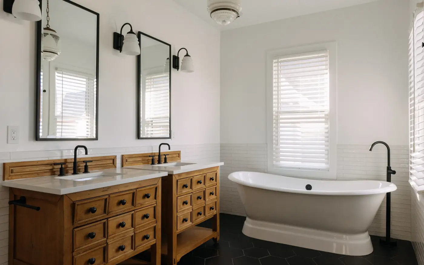 Bathroom with freestanding pedestal tub, wood double vanity and black hex floor — The Columbia Project
