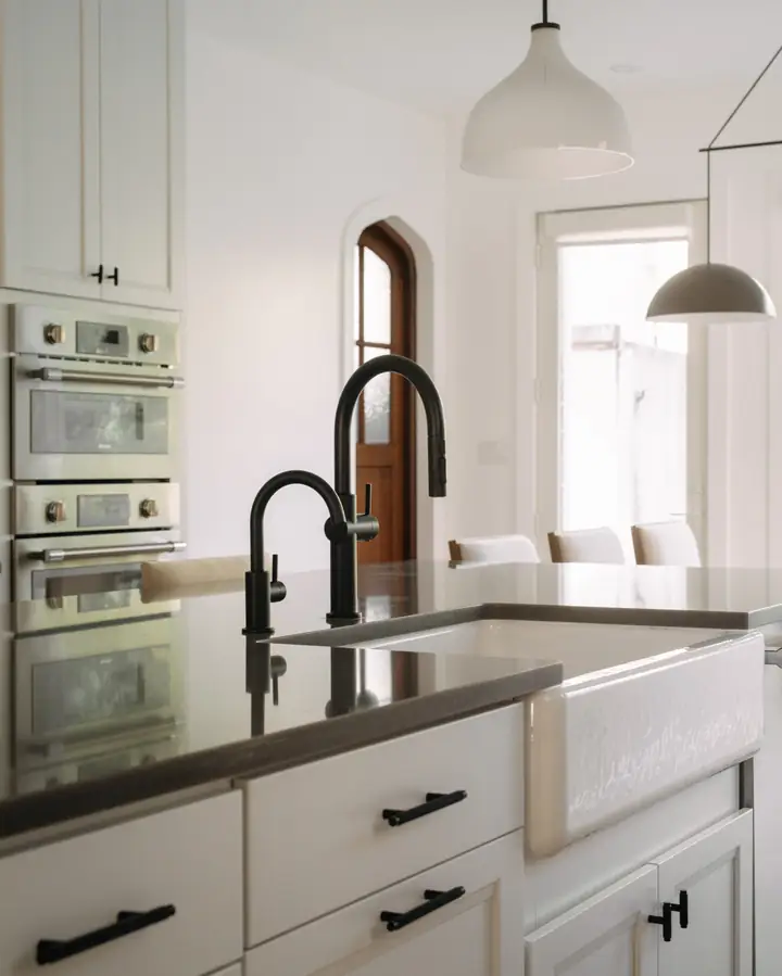 White kitchen with double wall ovens, farmhouse sink and matte black faucet — The Columbia Project